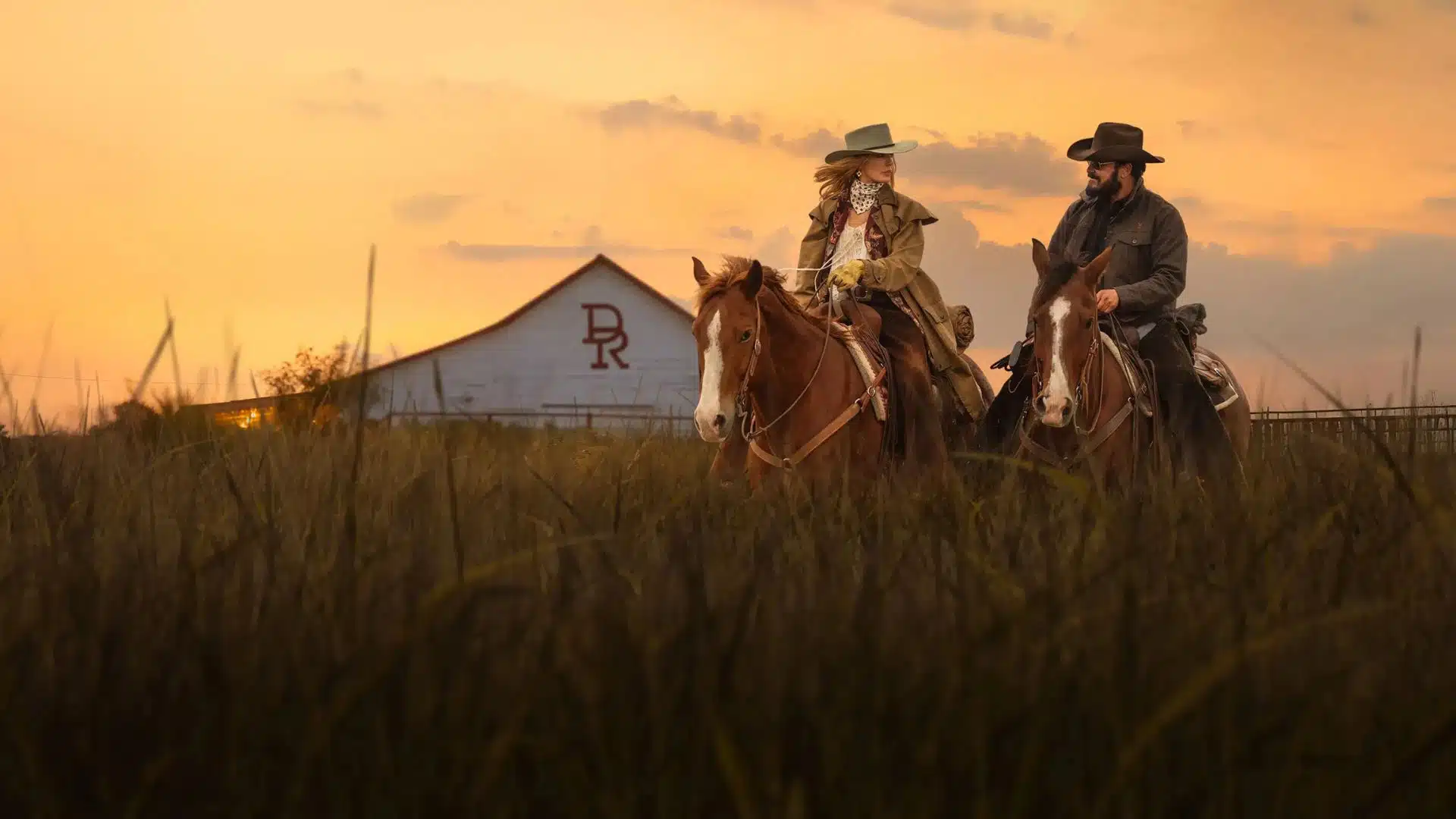 Kelly Reilly como Beth Dutton e Cole Hauser como Rip Wheeler a cavalo ao pôr do sol no Texas em cena de Rancho Dutton no Paramount+