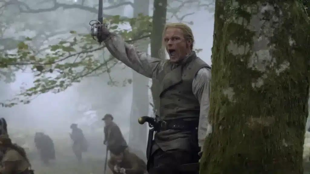 Sam Heughan como Jamie Fraser empunhando espada na Batalha de King's Mountain com soldados ao fundo no final da 8ª temporada de Outlander