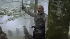 Sam Heughan como Jamie Fraser empunhando espada na Batalha de King's Mountain com soldados ao fundo no final da 8ª temporada de Outlander