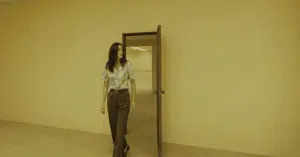 Corredor amarelado dos Backrooms com iluminação fluorescente e personagens perdidos no filme de terror da A24