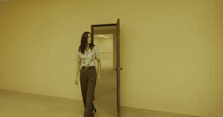 Backrooms: um Não-Lugar, por que o filme da A24 não confia na sua maior força Corredor amarelado dos Backrooms com iluminação fluorescente e personagens perdidos no filme de terror da A24