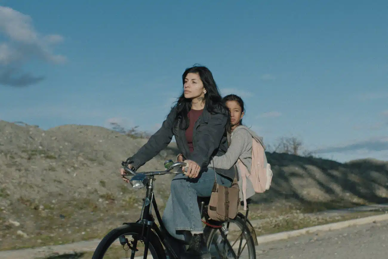 Cazzu como Sara e Elena Romero como Risa andando de bicicleta em paisagem de Ushuaia em cena de Risa e o Telefone do Vento na Netflix