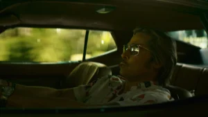 Brad Pitt como Cliff Booth ao volante em cena noturna da Hollywood de 1977