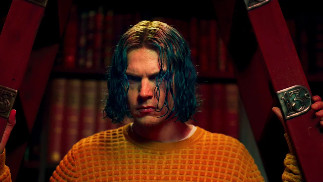 Evan Peters em American Horror Story 13 com expressão intensa, cabelo azul e número 13 ao fundo Evan Peters em American Horror Story 13 com expressão intensa, cabelo azul e número 13 ao fundo