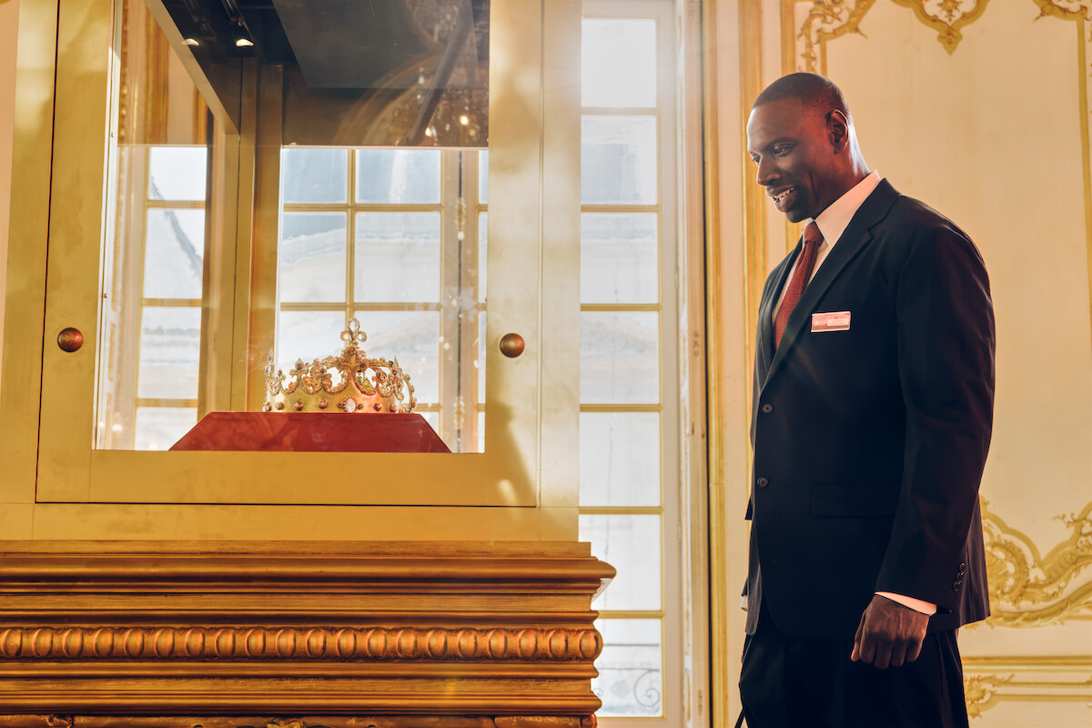 Personagem em terno examina coroa em vitrine de museu em Lupin